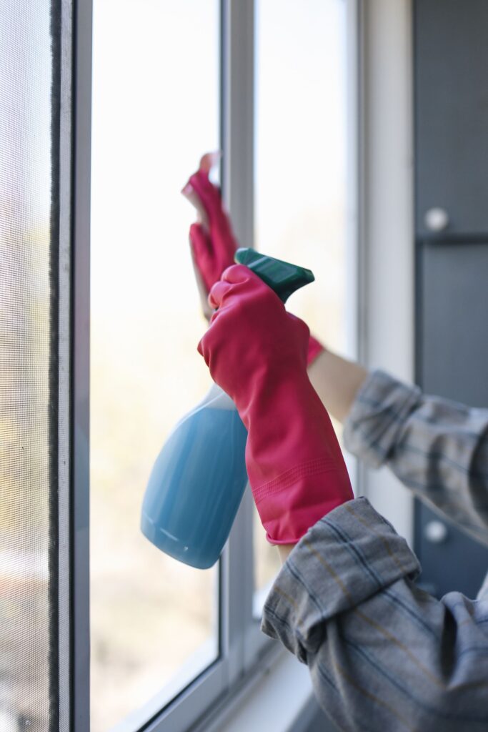 Reinigung eines Bürofensters - Person trägt pinke Handschuhe und sprüht mit einem Glasreiniger die Fenster an